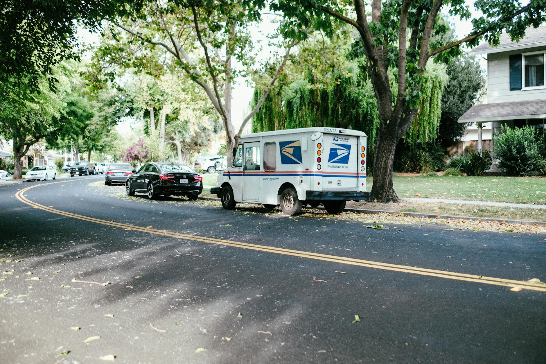 A postal delivery van parked on a tree-lined suburban street, showcasing daily mail service.